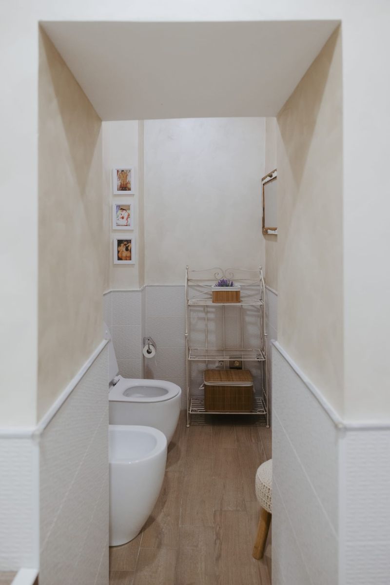 Bagno con sanitari sospesi, scaffale in ferro battuto bianco e cesto in vimini