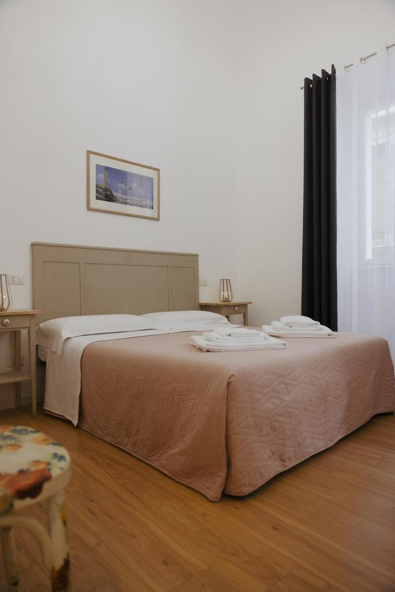 Letto matrimoniale della camera rosa con copriletto trapuntato, asciugamani piegati, comodini con lanterne e tende scure