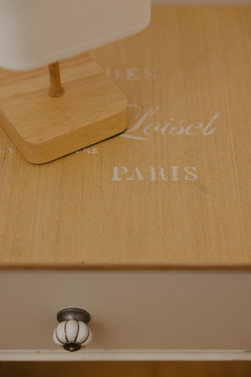 Dettaglio del piano del comodino in legno chiaro con la scritta a stencil e il pomello in ceramica